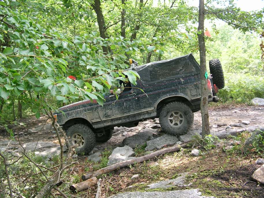 Dark off-road vehicle with large tires on a dirt path, surrounded by trees