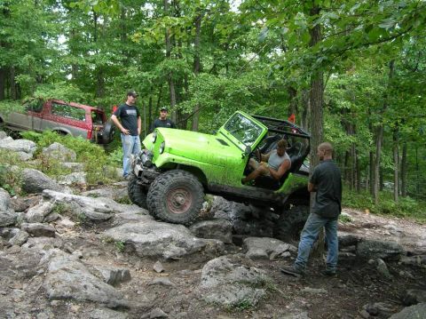1995 Ford Bronco - A bright green Jeep Wrangler tackles a challenging, rocky off-road path surrounded by dense foliage.