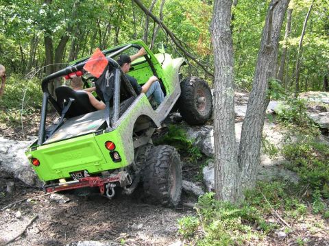 1995 Ford Bronco - A bright green Jeep navigates a challenging rocky terrain on a wooded trail.