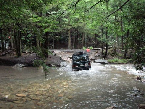 1995 Ford Bronco - An SUV navigates a rocky stream in a dense forest.