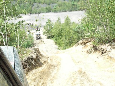 1995 Ford Bronco - Multiple SUVs navigate a challenging off-road trail in a wooded, hilly area.
