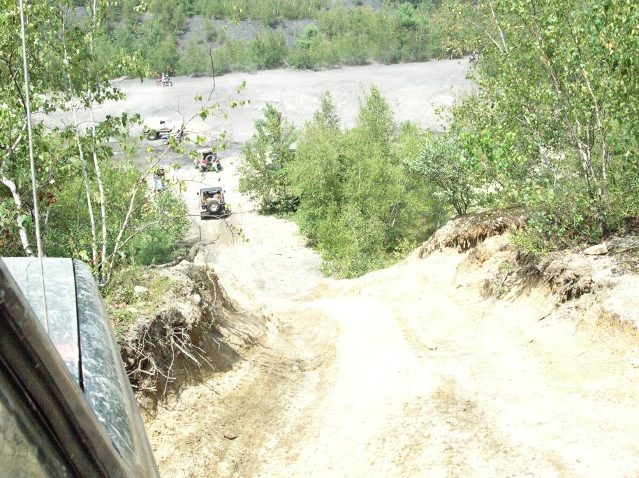 Off-road trail with several SUVs climbing a dirt hill. View from inside a vehicle