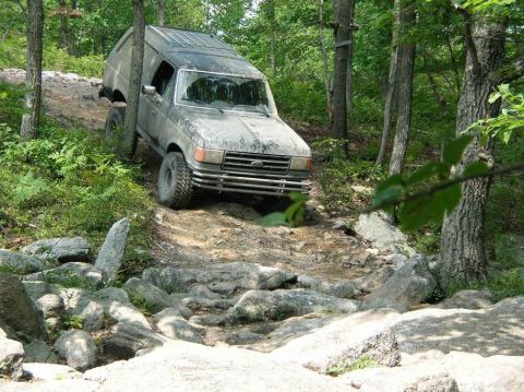 1995 Ford Bronco - A dusty Ford Bronco navigates a rocky, wooded path.