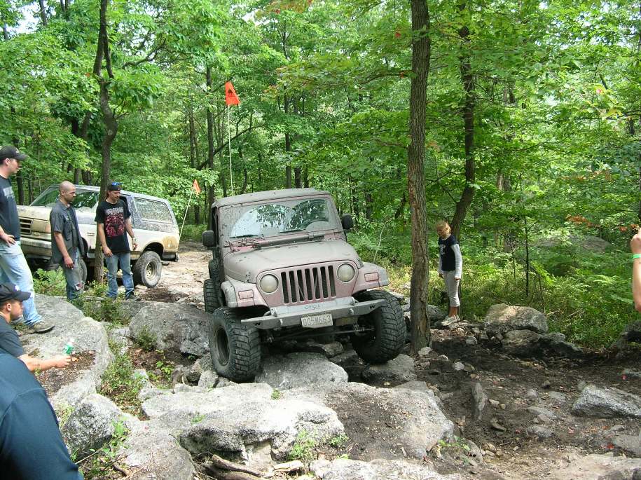 Tan Jeep Wrangler navigating rocks on a wooded trail