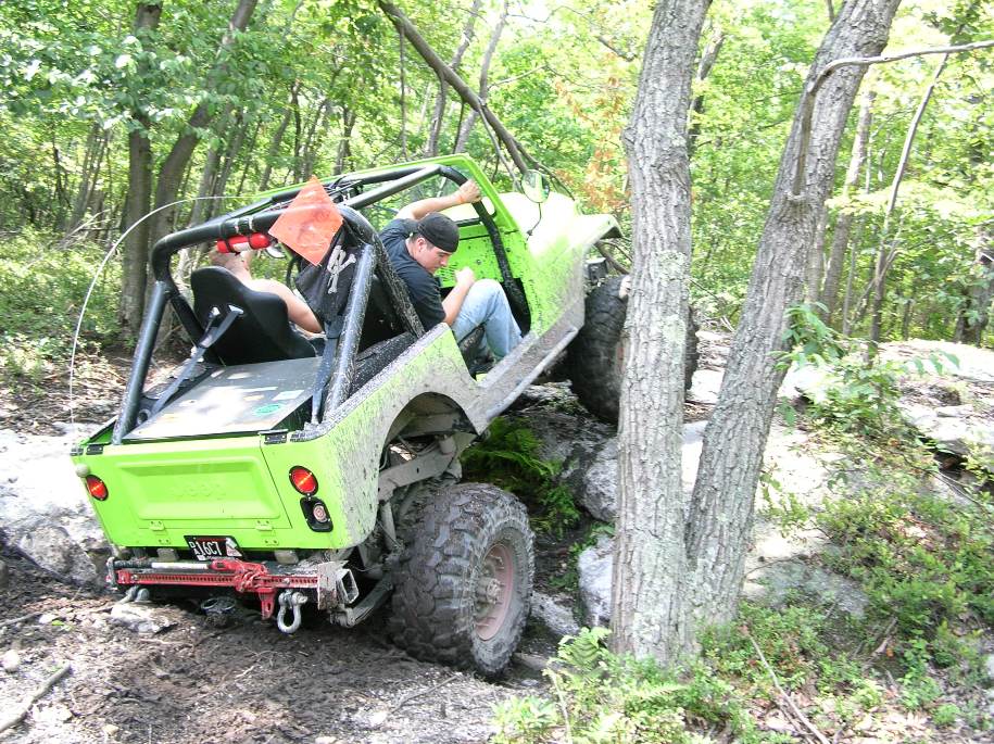 Lime green off-road vehicle with roll cage climbing over rocks and mud