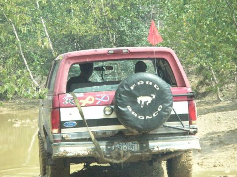 1995 Ford Bronco - This Ford Bronco, with a spare tire cover and a red flag, is navigating a muddy off-road trail.