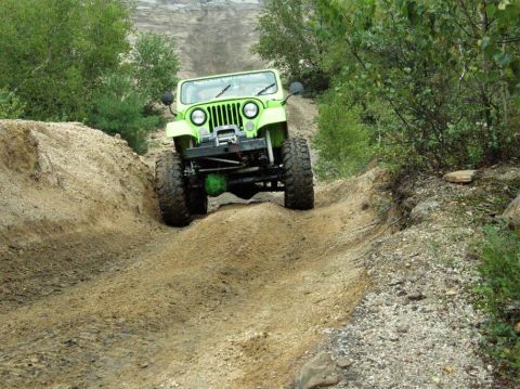 1995 Ford Bronco - A bright green off-road jeep navigates a challenging dirt track with steep inclines and loose gravel.