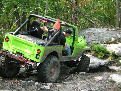 1995 Ford Bronco - A bright green Jeep navigates a challenging off-road course with rocky terrain and dense foliage.