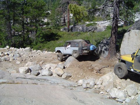 1967 Ford Bronco - A light-colored SUV navigates a challenging rocky terrain, with another yellow vehicle visible to the right.
