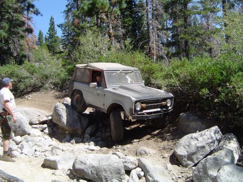 1967 Ford Bronco - A 1967 Ford Bronco navigates a challenging rocky off-road path with a person watching nearby.