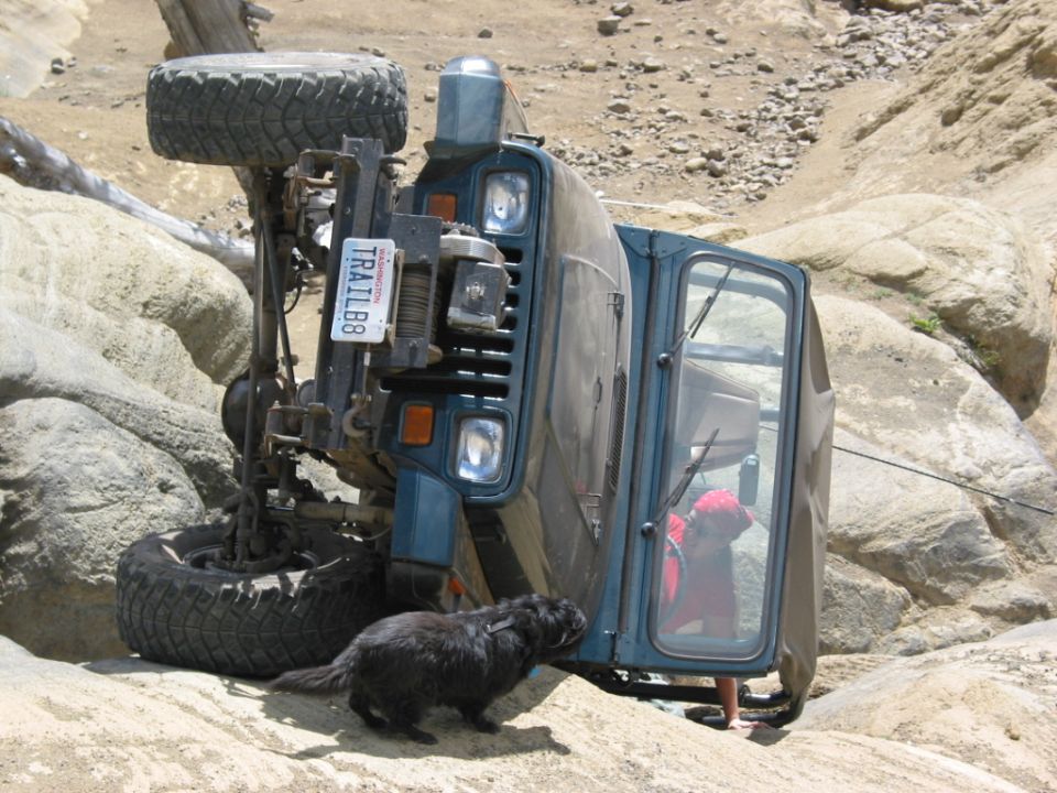 Blue Jeep Wrangler YJ on its side on rock, winch bumper and Washington TRAIL88 plate visible
