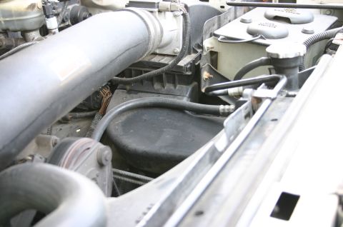 1994 Ford Bronco - Close-up of an engine bay showing a large gray intake tube, a black air filter housing, wiring harnesses, and a white plastic reservoir nea…