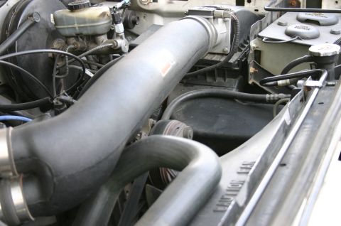 1994 Ford Bronco - Close-up of an engine bay showing large gray and black intercooler/intake piping routed across the engine, with a brake master cylinder res…
