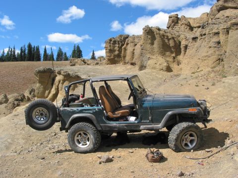 1982 Ford Customline - A green Jeep Wrangler sits on a dusty, rocky trail under a blue sky with scattered clouds.