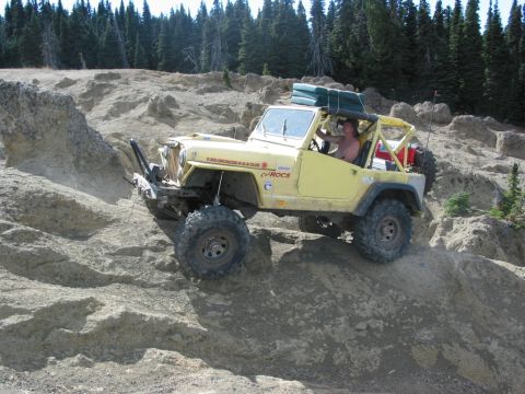 1982 Ford Customline - Off-roading Jeep navigating a steep, rocky incline with trees in the background.