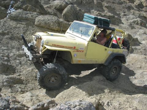 1982 Ford Customline - A yellow Jeep navigates a steep, rocky incline with a person driving and gear strapped to the roof.