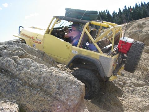 1982 Ford Customline - A yellow off-road vehicle navigates a rocky terrain with a spare tire mounted on the back.