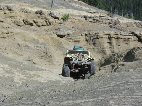 1982 Ford Customline - A yellow Jeep CJ-5 navigates a steep, rocky incline in a desolate, arid landscape.
