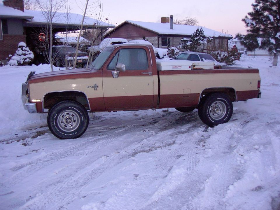 Two-tone brown and tan Chevy Silverado 4x4 pickup, side view, parked on a snowy street