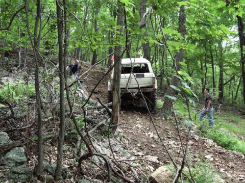 1995 Ford Bronco - A white SUV navigates a steep, muddy trail through a dense forest.