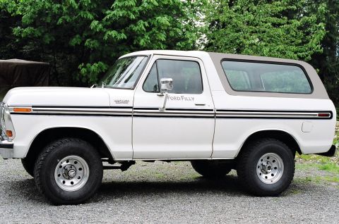 1979 Ford Bronco - A white 1978 Ford Bronco with a brown removable top is parked on a gravel surface with trees behind it.