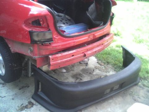 2005 Chevrolet Cavalier - The rear bumper of a red car has been removed, revealing damage to the car's frame and the detached bumper.