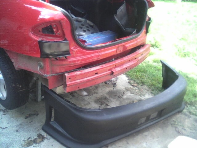 Red car with rear bumper removed, showing the damaged frame and removed black bumper on the ground