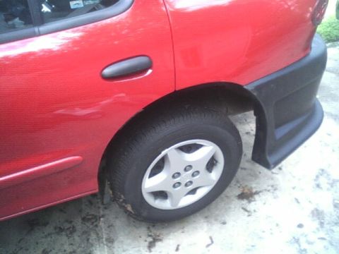2005 Chevrolet Cavalier - Rear quarter panel and wheel of a red 2005 Chevrolet Cavalier, showing its side profile and black body trim.