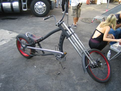 1968 Ford Mustang - A custom chopper bicycle with a long frame, red-rimmed wheels, and a black finish is parked outdoors.