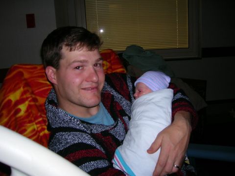 2003 Jeep TJ - A proud father cradles his newborn child, swaddled in a blanket and wearing a hospital hat.