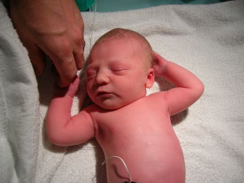 2003 Jeep TJ - A newborn baby rests on a white towel, with a hand gently holding its finger.