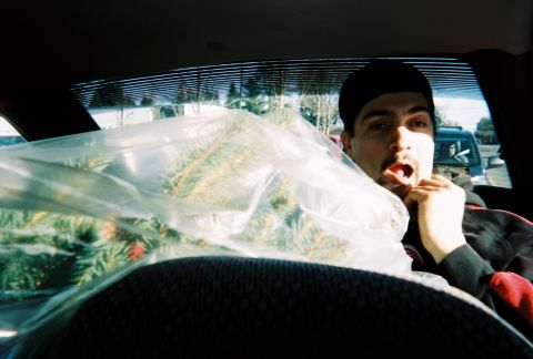 1990 Ford Bronco - A man is seen inside a vehicle, holding a large, plastic-wrapped Christmas tree. Another vehicle is visible through the rear window.
