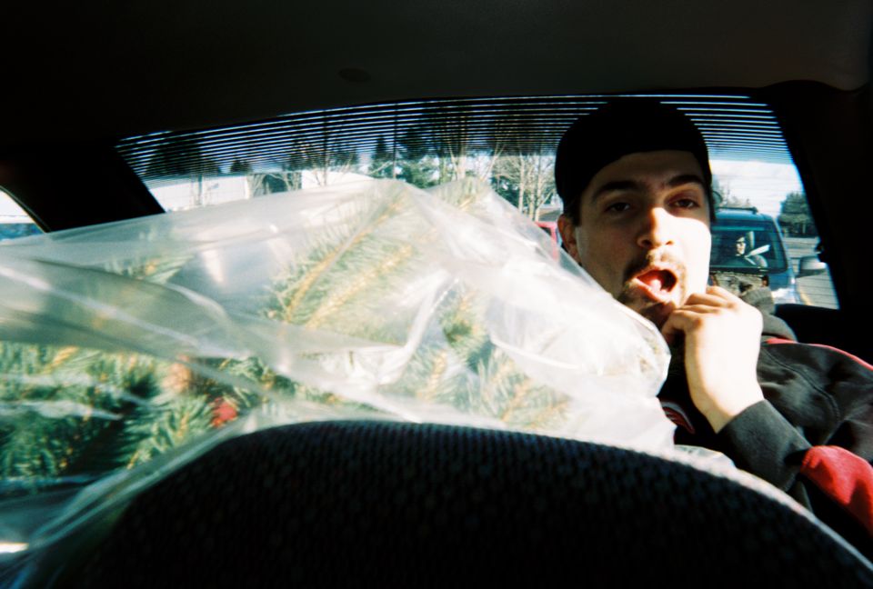 Man in car interior with Christmas tree; another vehicle visible outside