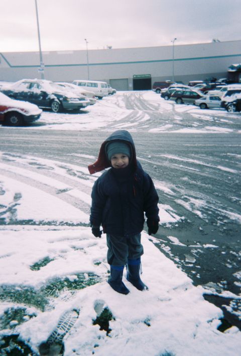 1990 Ford Bronco - A child stands in a snowy parking lot, with several vehicles visible in the background.