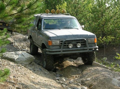 1995 Ford Bronco - A modified Ford Bronco is shown tackling a challenging off-road trail with a second vehicle in the background.