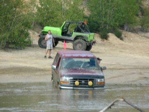 1995 Ford Bronco - A maroon 1995 Ford Bronco is stuck in the mud, with a green Jeep and a person standing nearby in the background.
