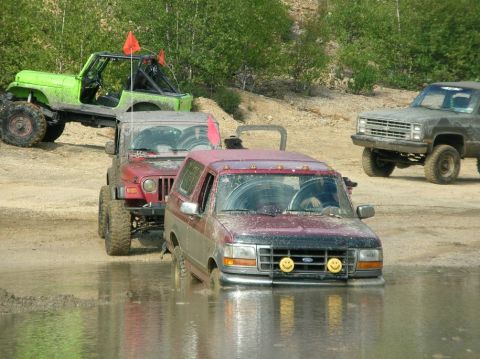 1995 Ford Bronco - Multiple off-road vehicles, including a 1995 Ford Bronco, navigate a muddy terrain.