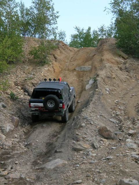 1995 Ford Bronco - Black SUV navigates a challenging off-road trail with steep inclines and loose terrain.