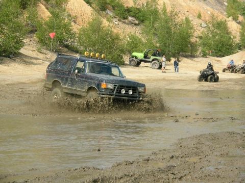 1995 Ford Bronco - A dark blue SUV navigates a muddy obstacle course, with other off-road vehicles visible in the background.