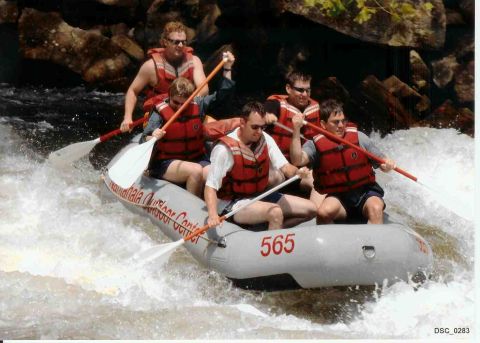 1985 Ford LTD Crown Victoria - A group of six people in a rafting boat navigate whitewater rapids, paddles in hand.
