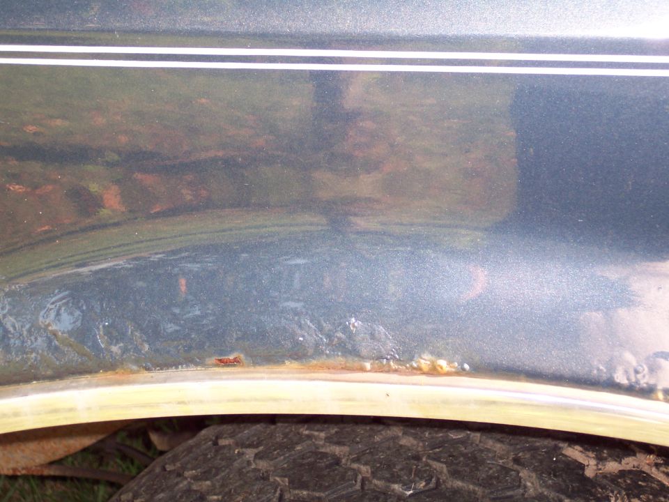 Close-up of rusted metal on a vehicle's wheel well with a tire visible below
