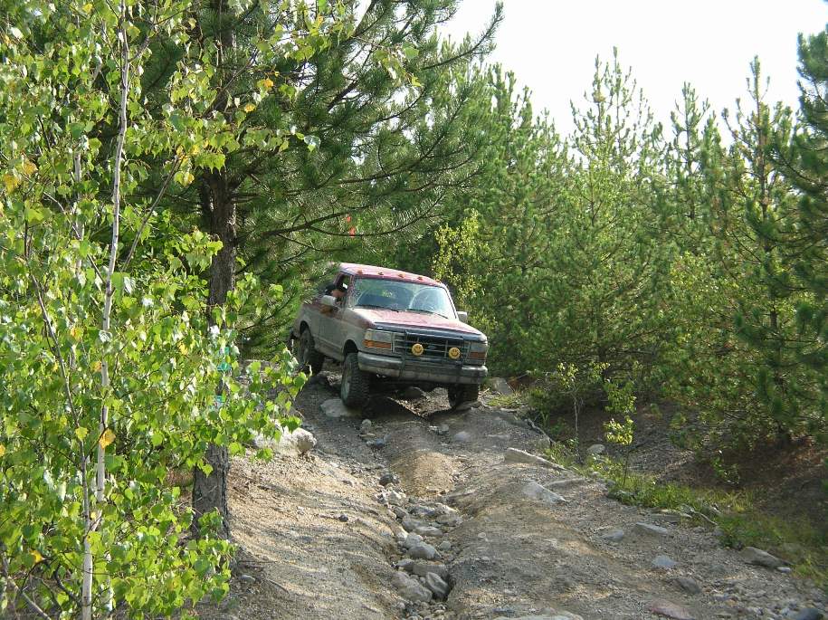 Red Ford Bronco driving on a rocky, wooded trail