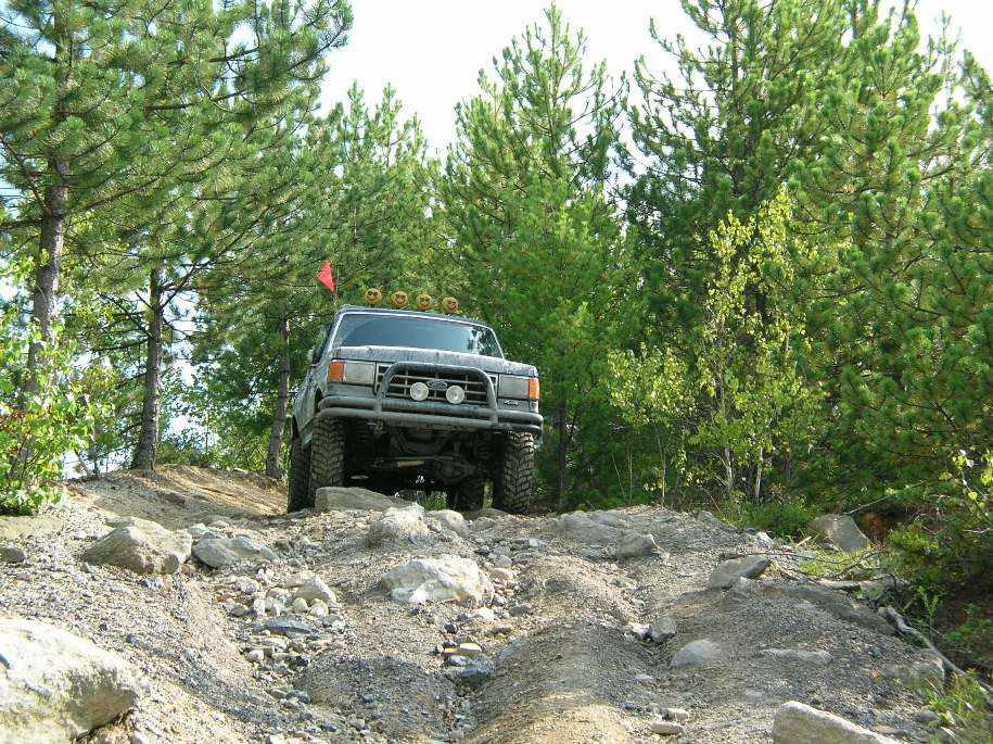 Gray Ford Bronco with off-road tires and a brush guard driving on a rocky trail