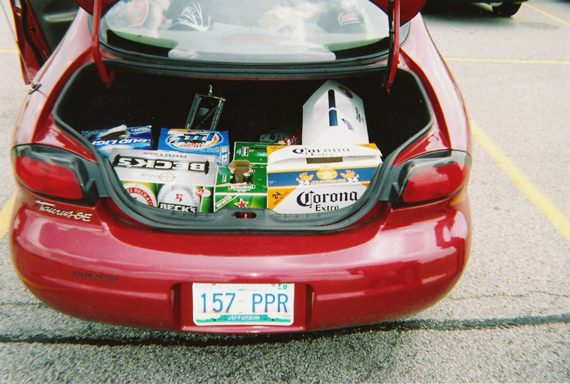 Trunk of a red car filled with boxes of Bud Light, Beck's, and Corona Extra beer