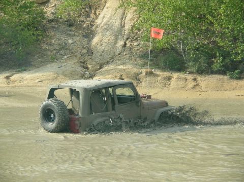 1995 Ford Bronco - A Jeep Wrangler navigates through a muddy terrain, kicking up water and mud.
