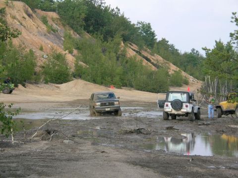1995 Ford Bronco - Off-road vehicles driving through a muddy area with a sandy hill and trees.