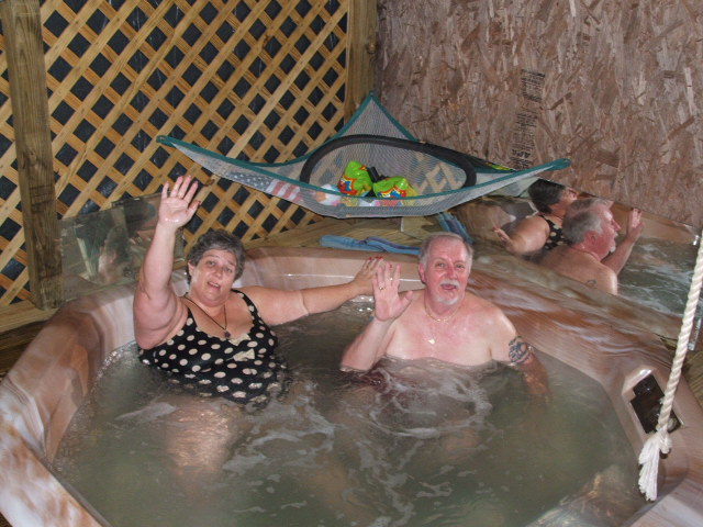 People waving from a hot tub with a hammock overhead
