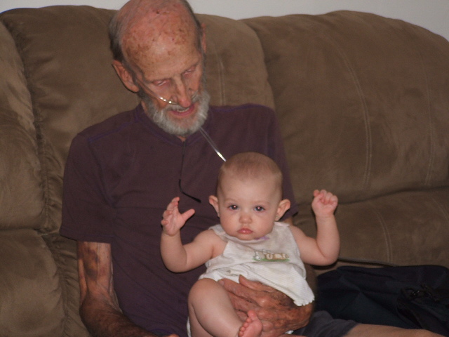 Man with oxygen tubes holding a baby on a couch