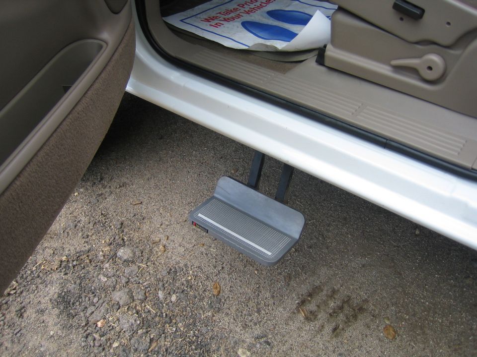 Deployed retractable power running board under open door of white pickup