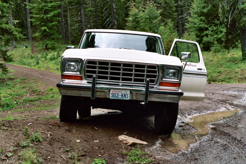 1979 Ford Bronco parked on a muddy dirt road in a forest, driver's door open